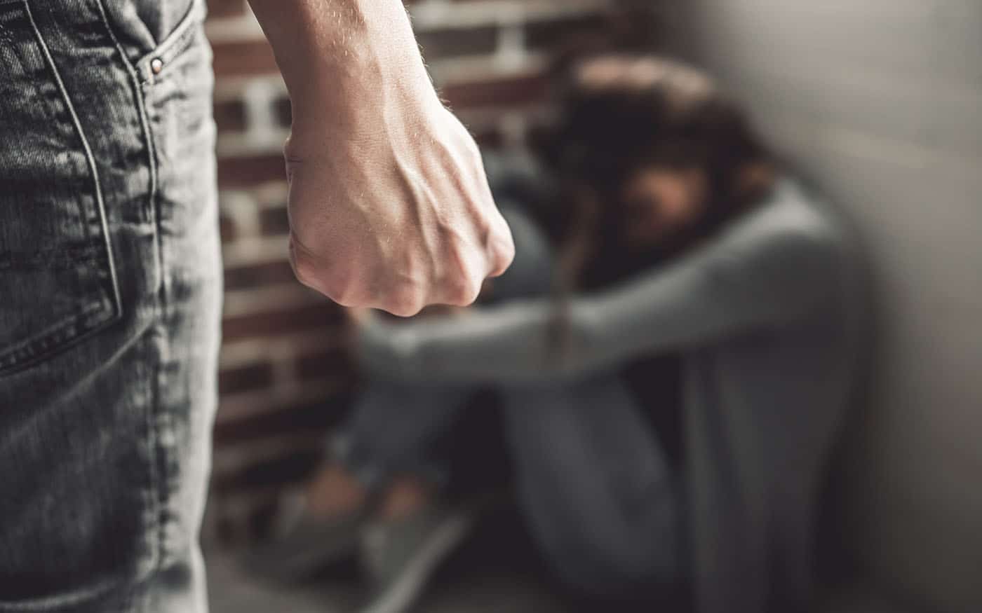 Femme frappÃ©e. Jeune fille assise sur le sol tandis que l'homme au premier plan serre le poing.